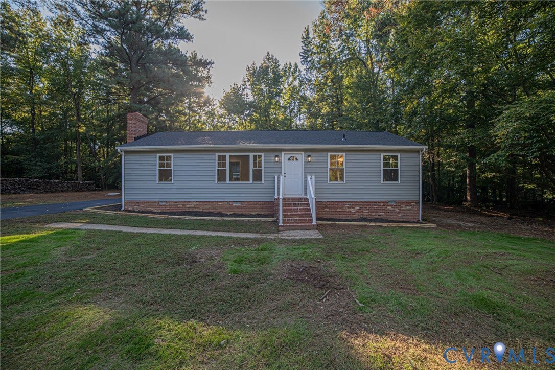 Single-story exterior with grey horizontal siding, a brick foundation, a chimney, and a concrete walkway