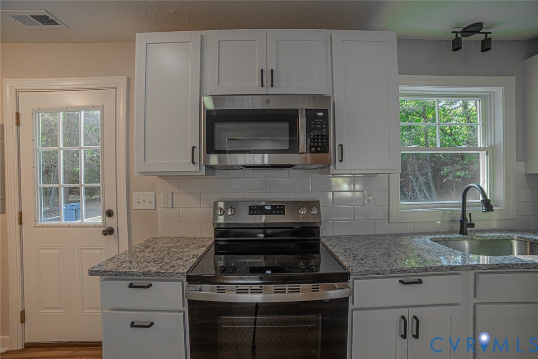 Kitchen featuring white shaker-style cabinetry, stone-patterned countertops, subway tile backsplash, stainless steel appliances, and a gooseneck faucet