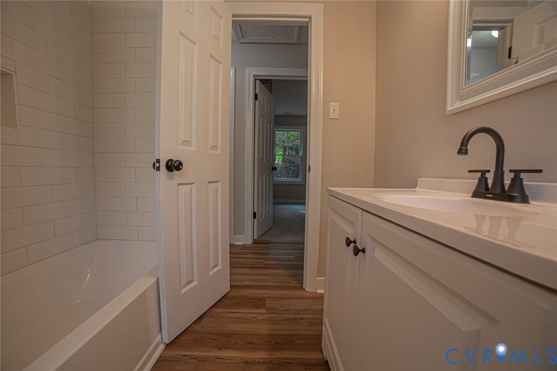 Bathroom featuring wood-finish flooring, white vanity with an integrated sink, matte black faucet, and a tub enclosure with white subway tile