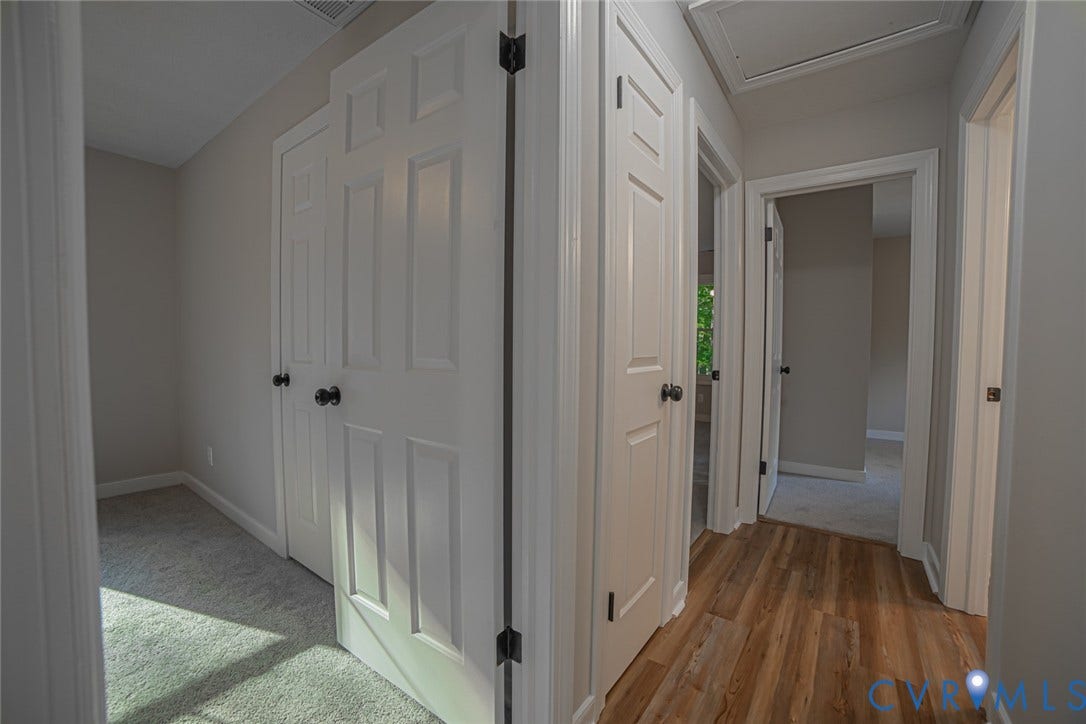 Hallway featuring neutral wall tones, multi-panel doors with matte black hardware, wood-finish flooring, and wall-to-wall carpeting