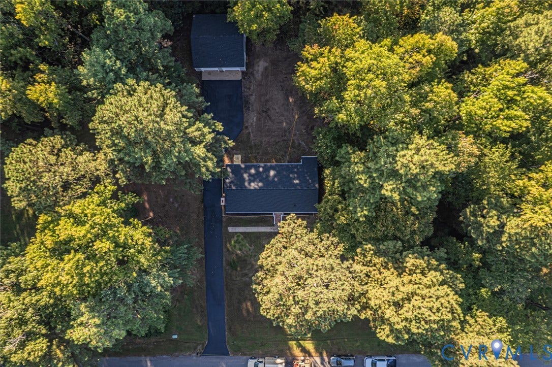 Aerial perspective featuring a detached garage, expansive asphalt driveway, and heavy mature tree canopy on a wooded lot
