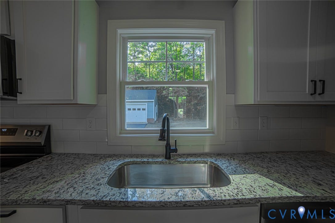 White cabinetry, stone-finish countertops, stainless steel undermount sink with a high-arc matte black faucet, and white subway tile backsplash