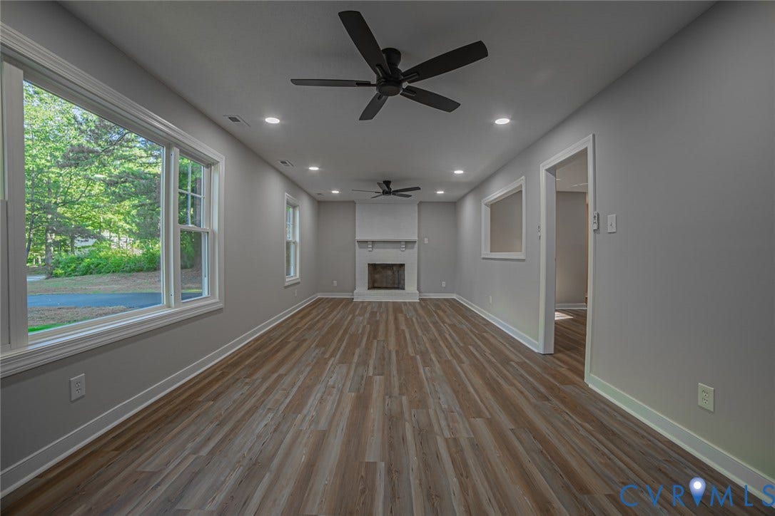 Neutral interior featuring wood-finish flooring, a white masonry fireplace, dual ceiling fans, recessed lighting, and large windows