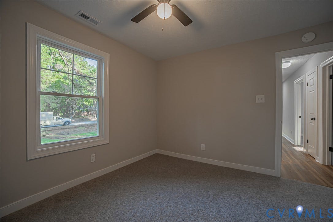 Neutral-toned interior featuring wall-to-wall carpeting, a multi-pane window with white trim, and a ceiling fan with integrated lighting