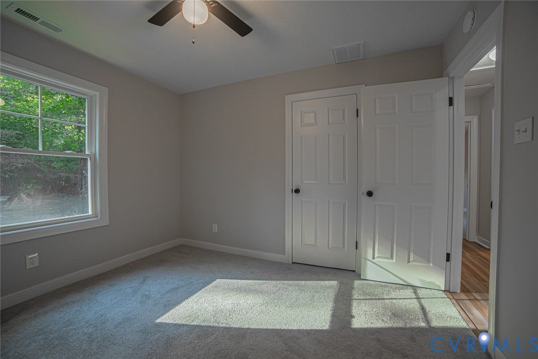 Interior space featuring neutral wall tones, plush wall-to-wall carpeting, a multi-panel interior door, and a ceiling-mounted light fixture with fan blades