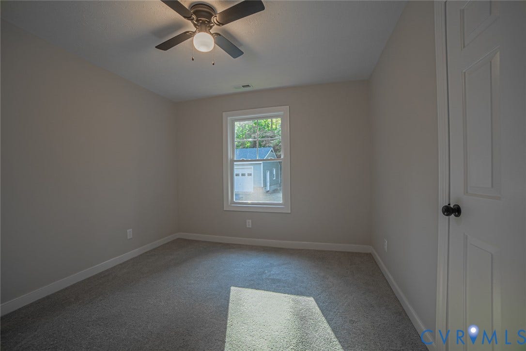 Neutral-toned interior space featuring wall-to-wall carpeting, a single-hung window, a ceiling fan with integrated light fixture, and a paneled door with a round knob