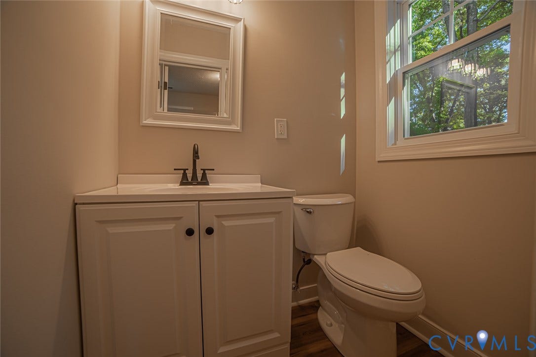 White cabinetry featuring a built-in vanity, neutral countertop, dark finish hardware, and wood-finish flooring