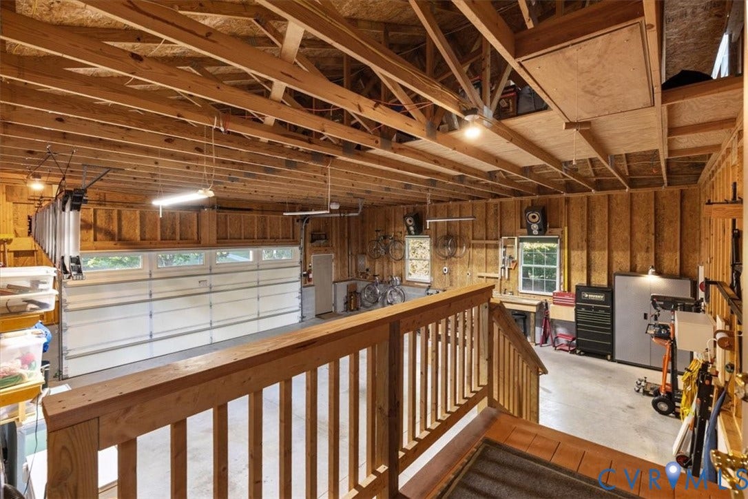 5111 Hurop Road, Sandston, VA 23150 Multi-vehicle garage featuring exposed wood truss ceiling, concrete flooring, overhead linear lighting, and a wooden balcony railing