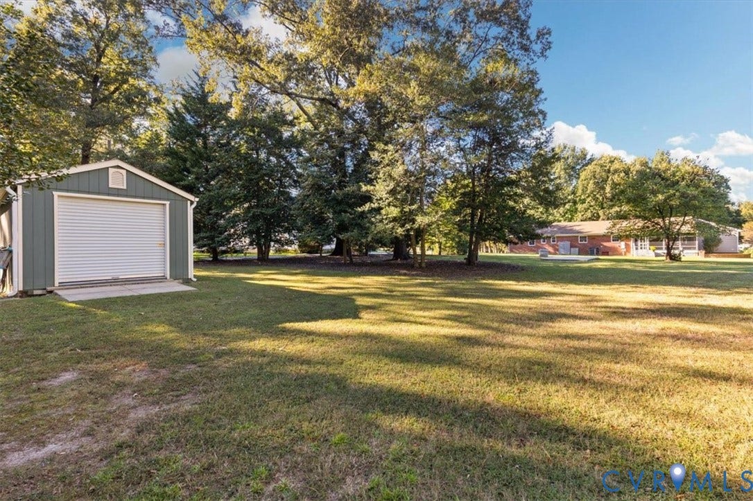 5111 Hurop Road, Sandston, VA 23150 Spacious backyard featuring a detached garage with a roll-up door, mature trees, and an open lawn area
