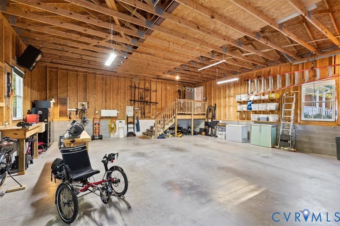 5111 Hurop Road, Sandston, VA 23150 Spacious multi-car garage featuring exposed wood truss ceiling, concrete flooring, dual double-hung windows, and an elevated wood staircase with balustrades