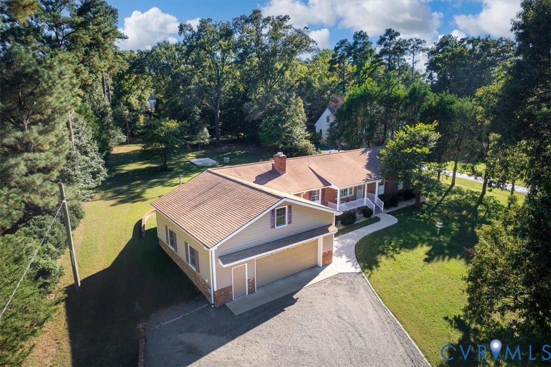5111 Hurop Road, Sandston, VA 23150 Exterior featuring a shingle roof, beige siding, brick masonry detailing, and a multi-car garage on a landscaped lot with mature trees