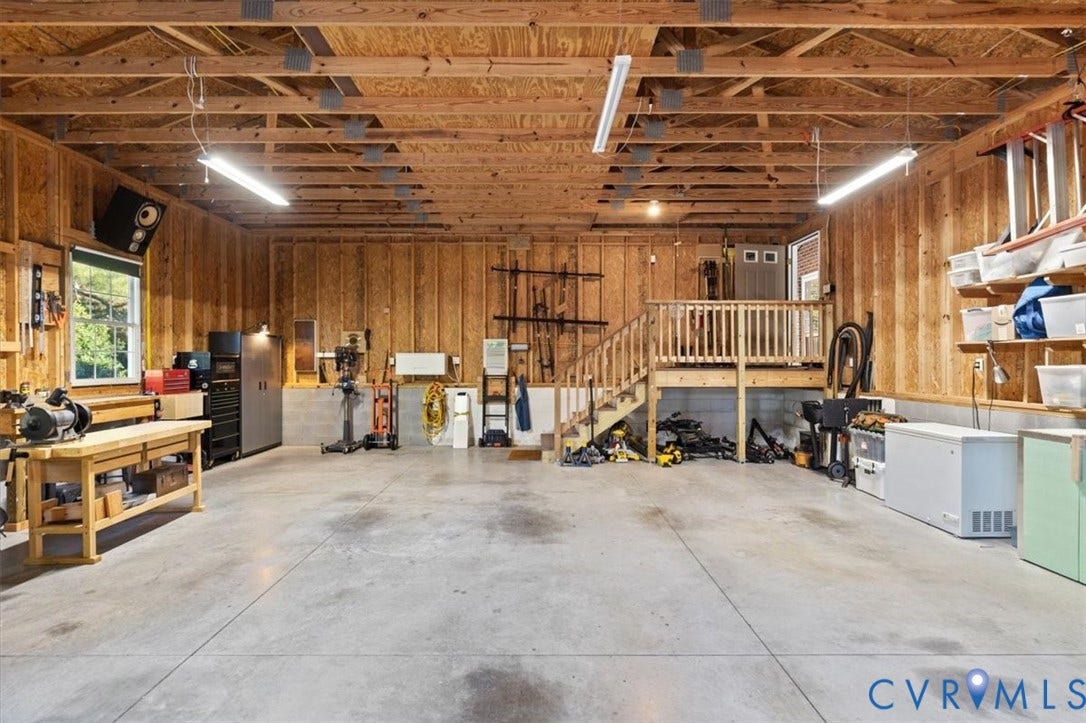 5111 Hurop Road, Sandston, VA 23150 Oversized garage featuring exposed wood-stud walls, concrete flooring, linear fluorescent lighting, and an elevated wooden platform with integrated staircase