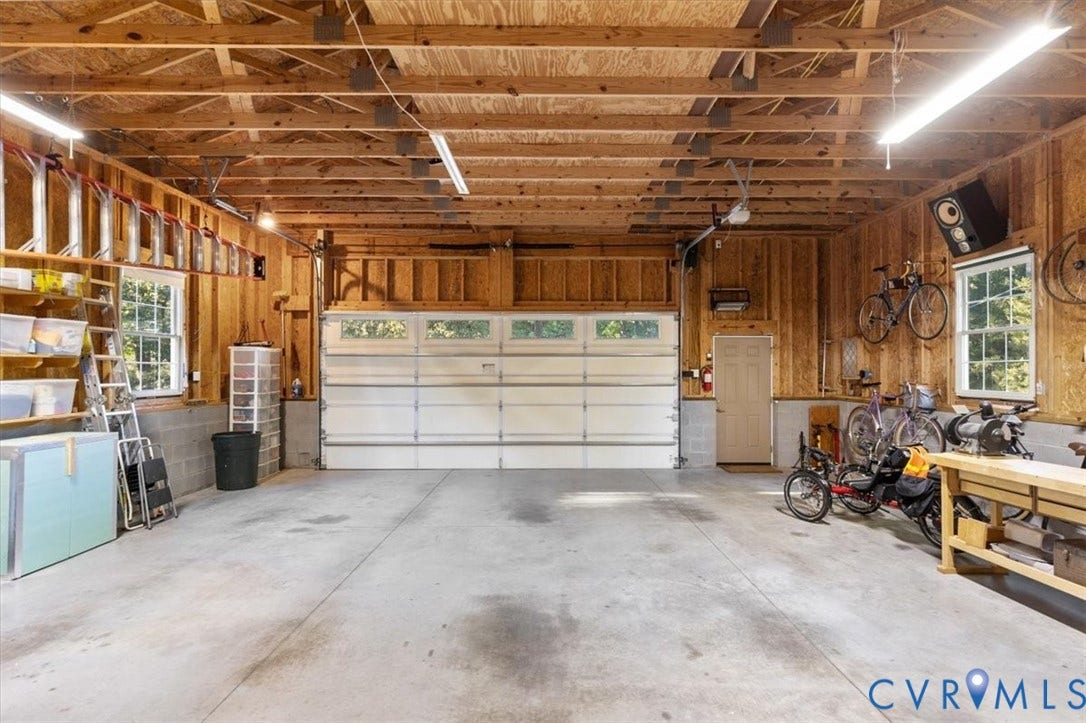 5111 Hurop Road, Sandston, VA 23150 Spacious garage featuring concrete flooring, exposed wood framing, multi-pane sectional overhead door, dual windows, and linear fluorescent lighting