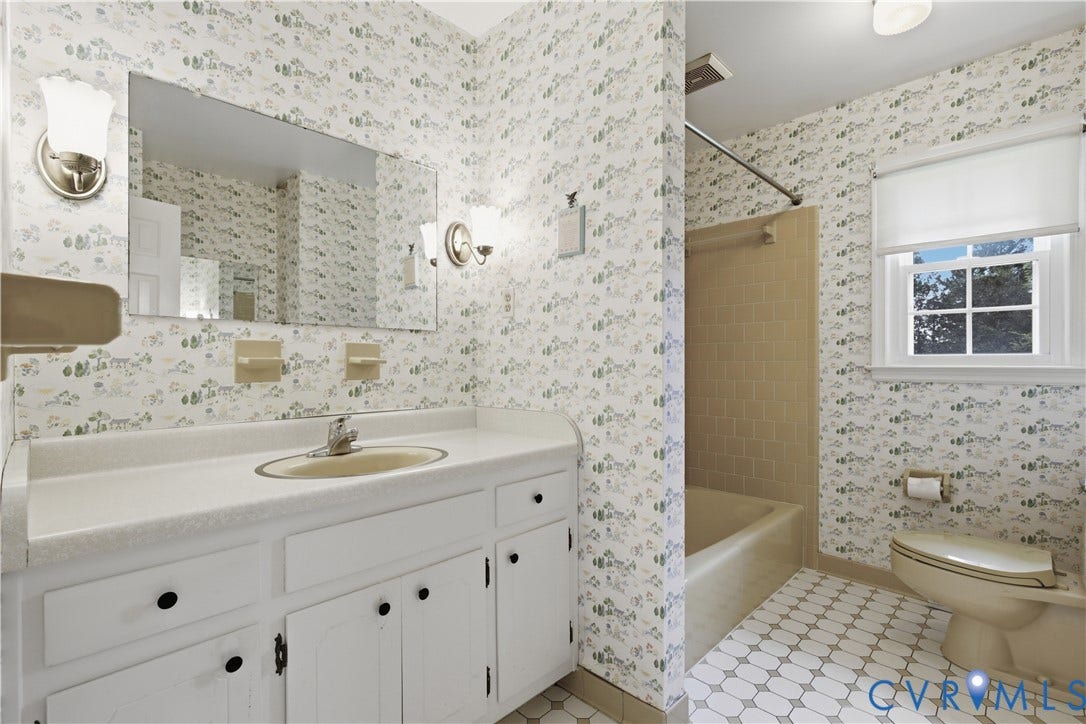 3641 Kiefer Road, Bermuda, Chester, VA 23831 Bathroom featuring a white vanity with an integrated basin, a rectangular wall-mounted mirror, dual metallic sconce lighting, and a tiled tub enclosure