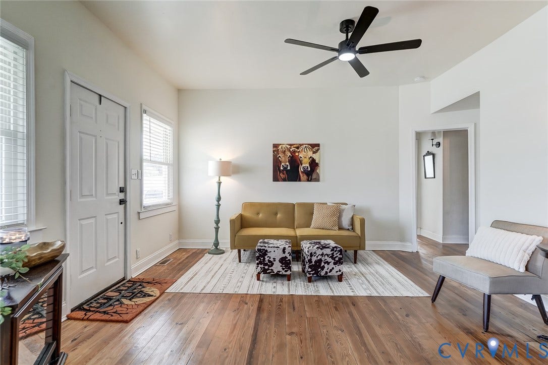 Living area featuring wood-finish flooring, multi-pane windows, and a matte black ceiling fan with integrated lighting
