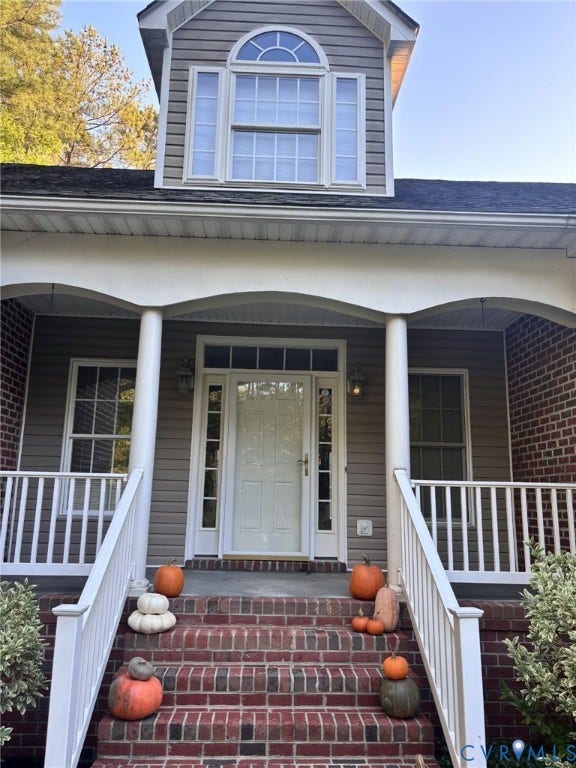 Covered front porch featuring a brick staircase, white balustrades, arched structural pillars, and a multi-pane entry door with sidelights and transom window