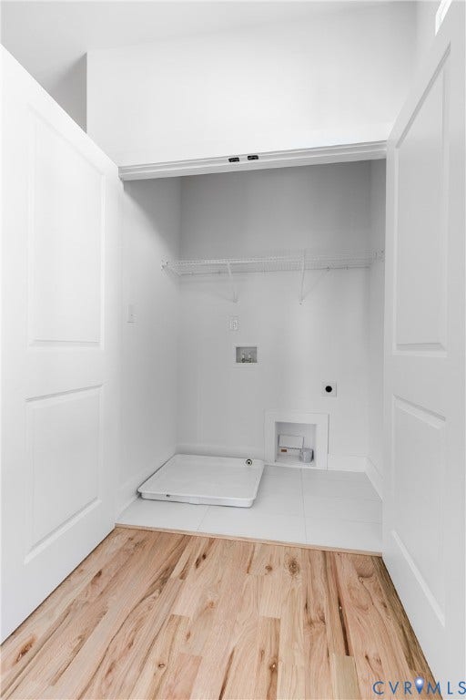 Dedicated utility closet featuring white tile flooring, wood-finish flooring in the exterior area, double-panel swing doors, a metal wire shelf, and a built-in floor basin