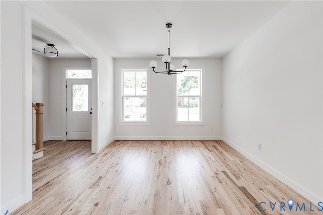 Bright interior featuring wood-finish flooring, two double-hung windows, a tiered multi-globe chandelier, and an exterior door with a transom window