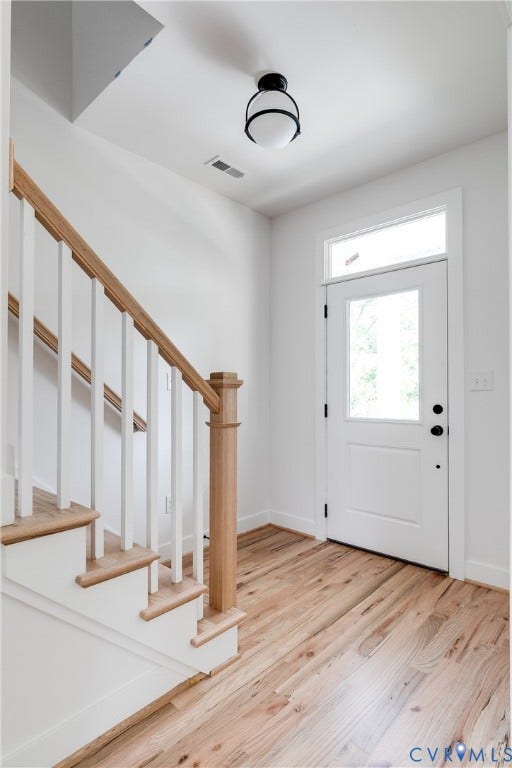 Foyer featuring wood-finish flooring, a white paneled door with a transom window, and a staircase with a natural wood handrail and square balusters