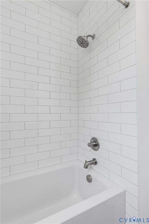 Bathtub enclosure featuring white subway tile wall surround, brushed nickel shower head, matching tub spout, and integrated mixing valve