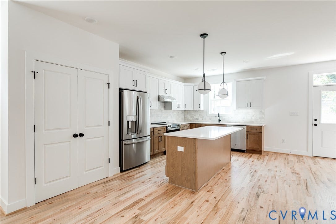 Kitchen featuring white upper cabinetry, lower wood-finish cabinetry, an island with a light-colored countertop, stainless steel appliances, and wood-finish flooring