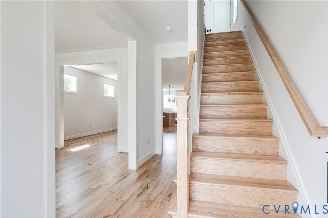 Staircase featuring light-toned wood treads and a matching handrail with a decorative newel post, complemented by wood-finish flooring throughout the entry area