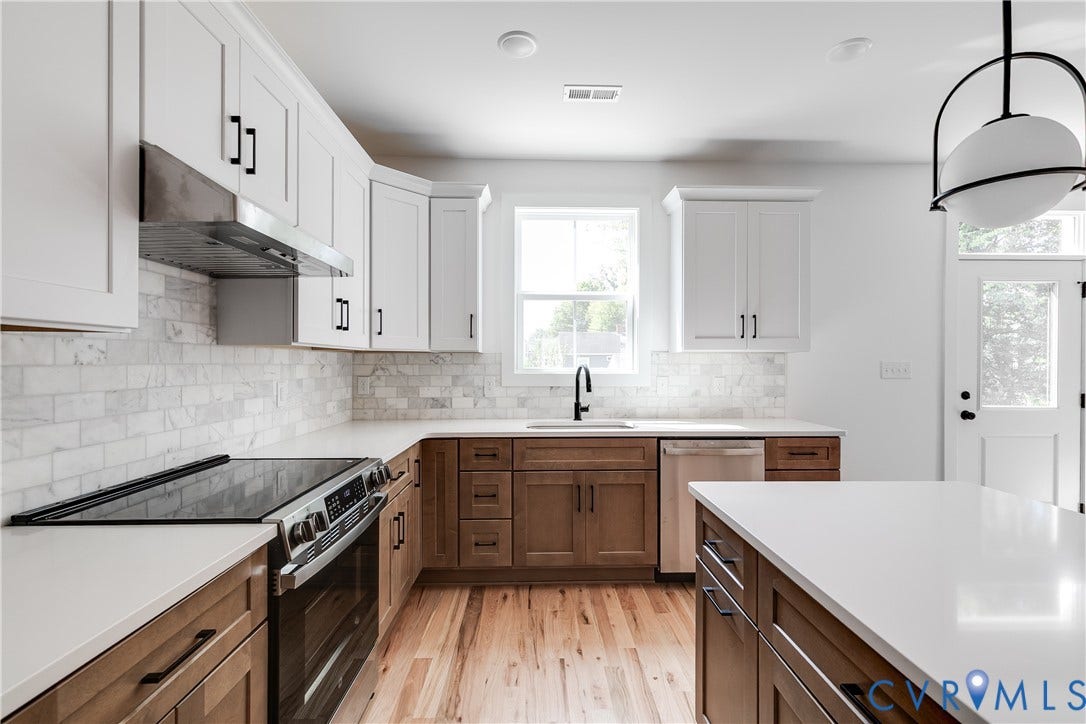 Kitchen featuring two-tone cabinetry, stone tile backsplash, white quartz countertops, stainless steel appliances, and wood-finish flooring