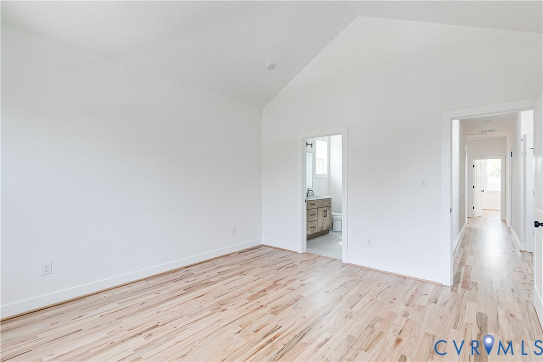 Room featuring vaulted ceilings, light-toned wood-finish flooring, and crisp white wall paint