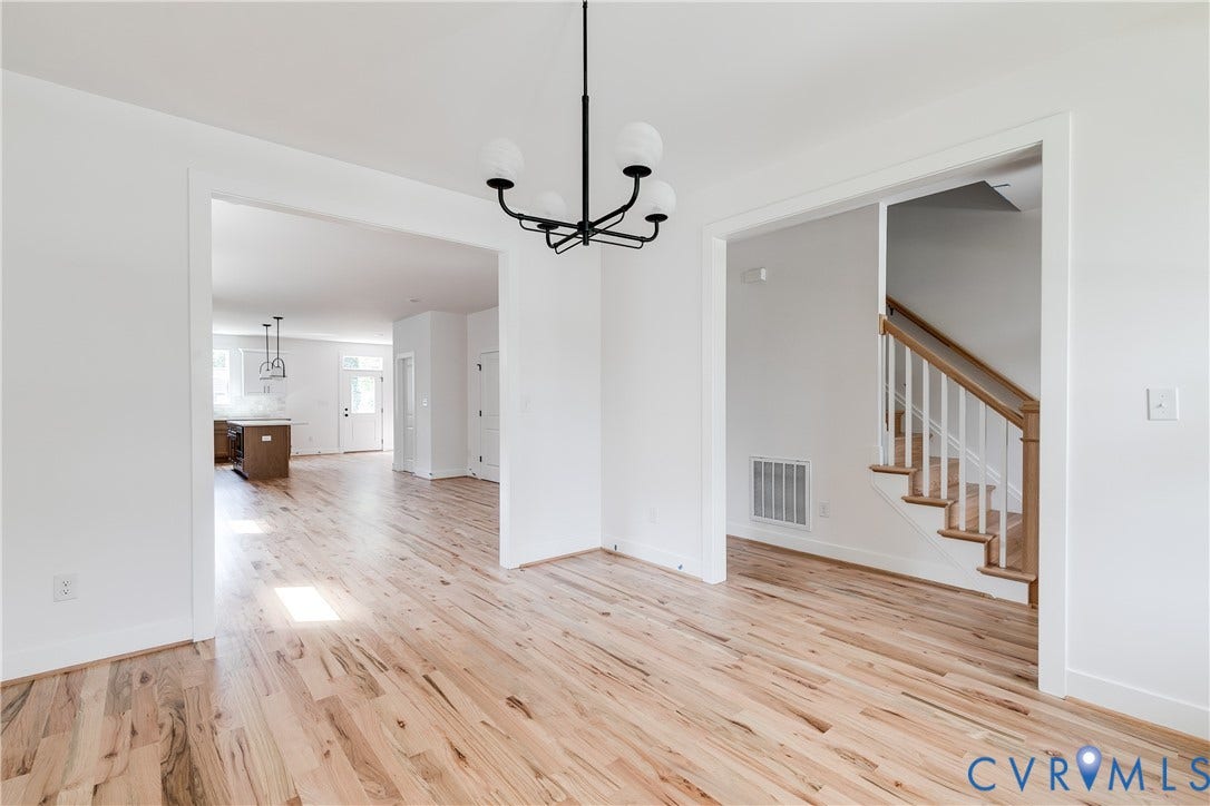 Wood-finish flooring throughout, matte black multi-light chandelier, and staircase featuring white balusters with a natural wood-tone handrail