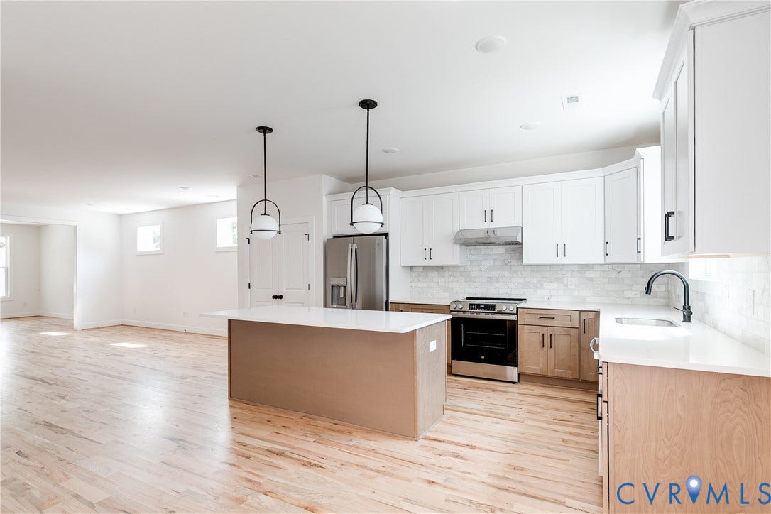 Kitchen featuring white upper cabinetry, lower wood-finish cabinetry, an oversized center island with quartz countertops, two modern globe pendant lights, and stainless steel appliances