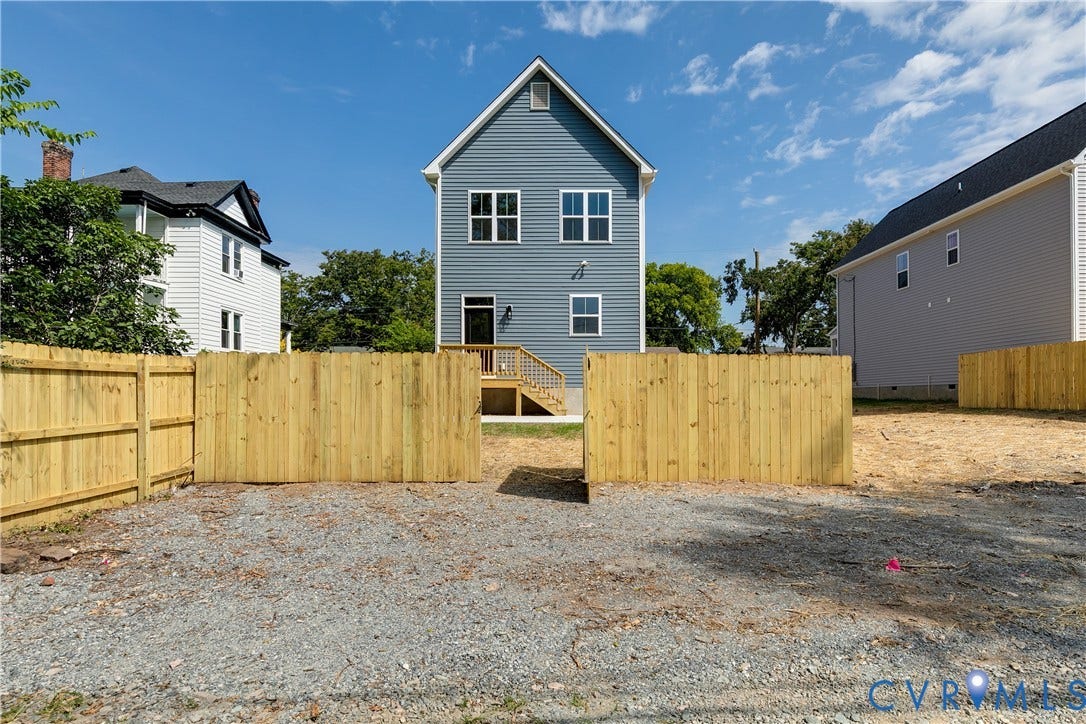 Two-story residence with horizontal siding, a gable roofline, elevated rear wood deck, and a fenced backyard area featuring gravel surfacing