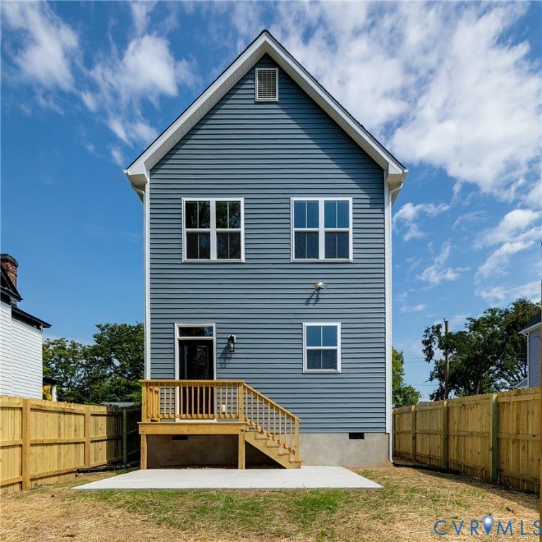 Two-story exterior featuring blue horizontal siding, a rear wood deck with stairs, a concrete patio, and perimeter wood privacy fencing