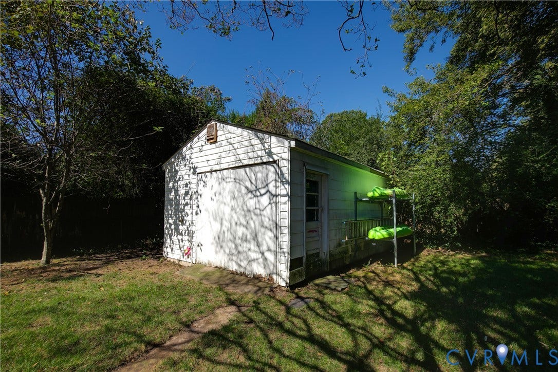 2108 Parkside Avenue, Henrico, VA 23228 Detached single-car garage featuring white siding, a metal overhead door, and a side-entry pedestrian door, situated on a grass-covered lot with mature trees