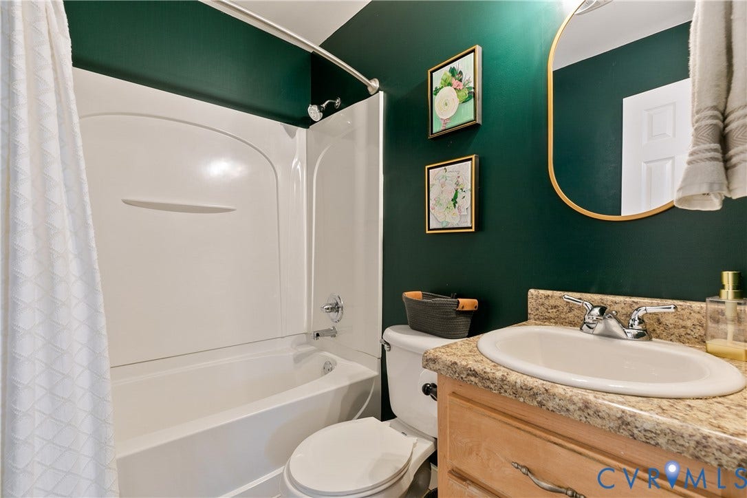 2108 Parkside Avenue, Henrico, VA 23228 Bathroom featuring a white molded tub-and-shower surround, stone-composite countertop, light-wood cabinetry, and arched wall mirror with a metallic frame