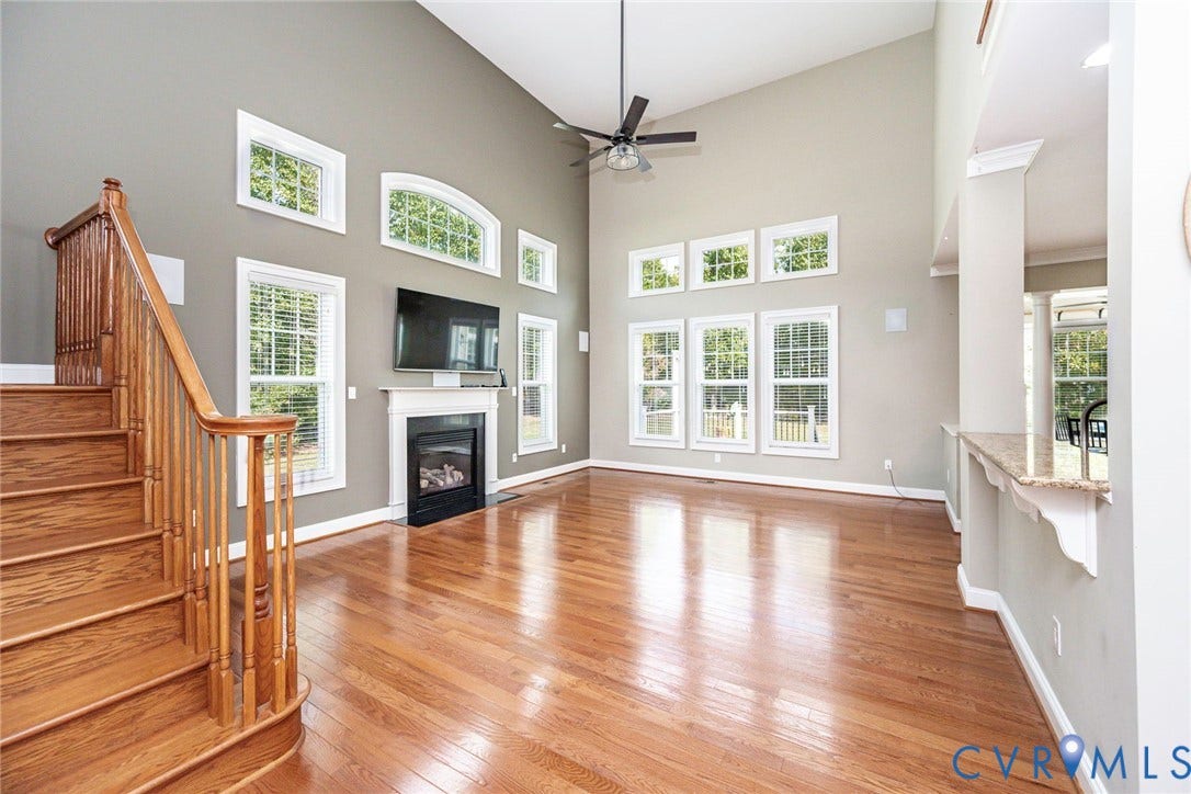 9118 Colonnade Circle, Ashland, VA 23005 Vaulted ceilings featuring a central fan, hardwood flooring, multi-level windows, a gas fireplace with a decorative mantel, and a wooden staircase with a baluster railing