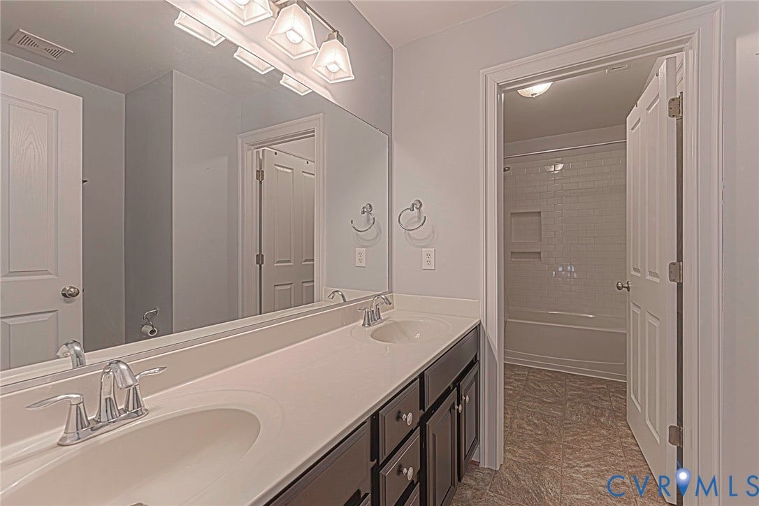 9118 Colonnade Circle, Ashland, VA 23005 Dual-sink vanity with a solid-surface countertop, full-width mirror, multi-light fixture, and recessed tub-shower combination with tile surround
