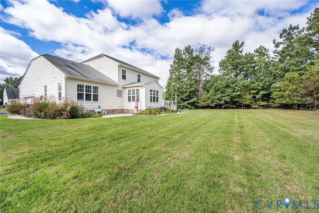 9118 Colonnade Circle, Ashland, VA 23005 Expansive backyard featuring a manicured lawn, perimeter mature trees, light-toned horizontal siding, multi-gabled roofline, and concrete patio
