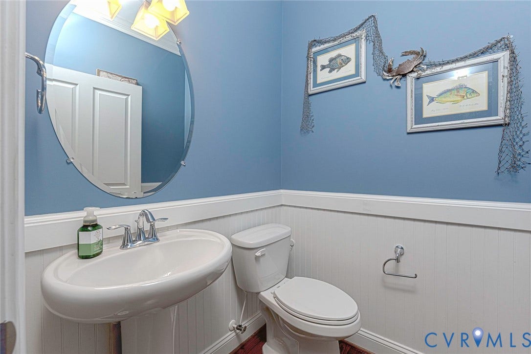 9118 Colonnade Circle, Ashland, VA 23005 Oval frameless mirror, white pedestal sink with chrome dual-handle faucet, wainscoting, and polished metal hardware
