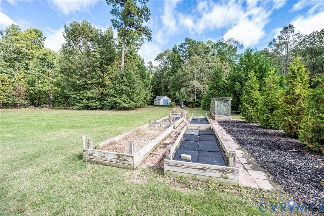 9118 Colonnade Circle, Ashland, VA 23005 Backyard featuring wood-frame raised garden beds, manicured lawn, established perimeter trees, and a detached storage structure
