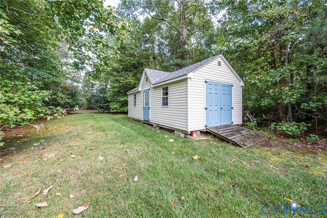 9118 Colonnade Circle, Ashland, VA 23005 Detached outbuilding featuring vinyl siding, shingled gable roof, double door entry, and wooden accessibility ramp, situated on a grass-covered lot with mature trees