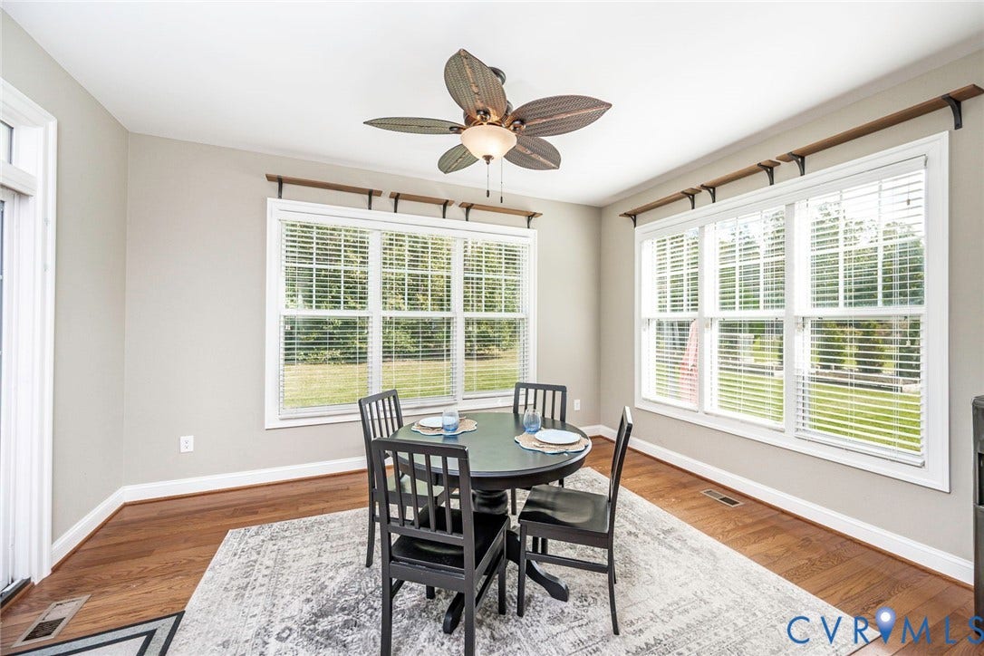 9118 Colonnade Circle, Ashland, VA 23005 Wood-finish flooring, ceiling fan with integrated light fixture, and multiple large windows featuring horizontal blinds and decorative wall-mounted shelving brackets