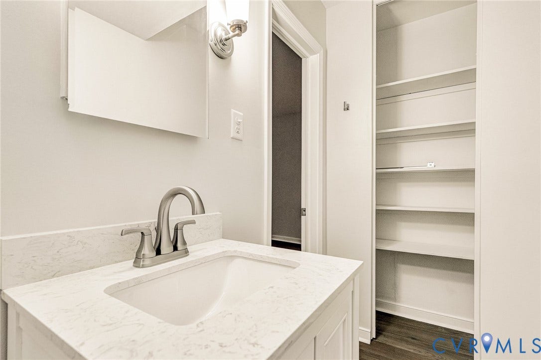 4 Millstone Road, The Hamlet, Henrico, VA 23228 Vanity featuring a stone-composite countertop with an integrated rectangular sink and brushed-nickel faucet, complemented by a wall-mounted light fixture, frameless mirror, and built-in shelving unit