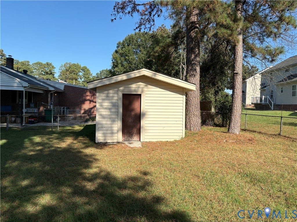 106 Verbov Avenue, Lundsford, Colonial Heights, VA 23834 Detached storage building with horizontal siding and a single entry door, situated on a lot featuring mature trees and a chain-link perimeter fence