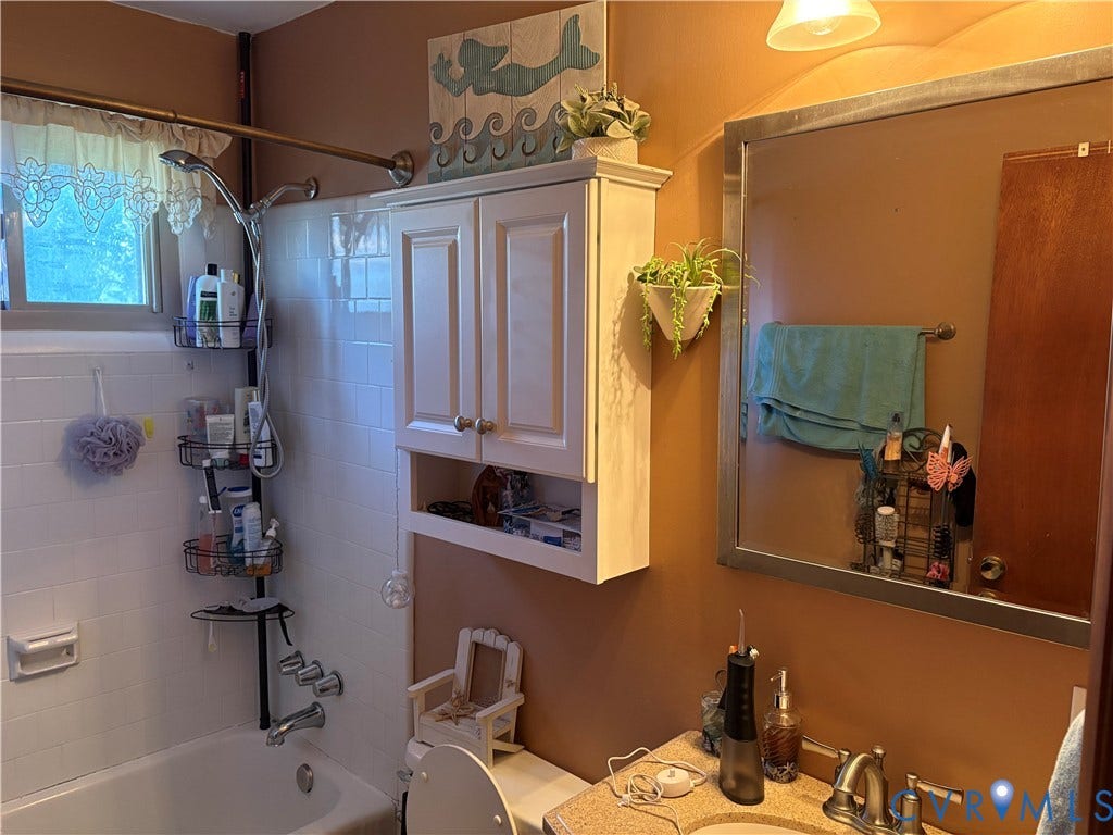 106 Verbov Avenue, Lundsford, Colonial Heights, VA 23834 Bathroom featuring white subway tile tub surround, built-in white wall cabinetry, rectangular vanity mirror with metallic frame, and chrome-finish sink fixtures