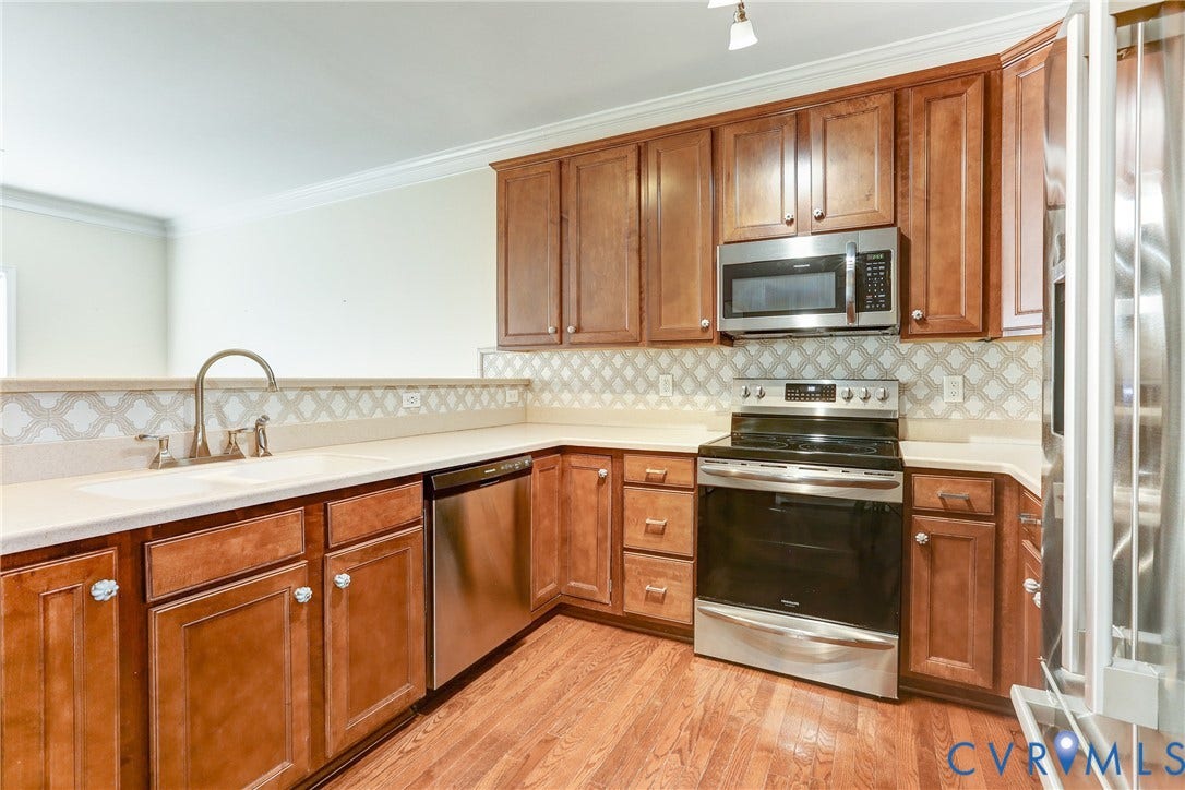 Kitchen featuring stained wood cabinetry, stainless steel appliances, patterned tile backsplash, solid-surface countertops, and wood-finish flooring