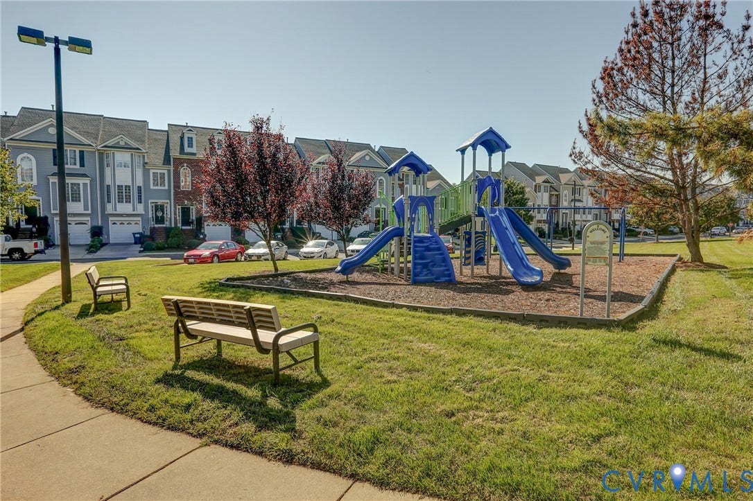 Community playground featuring multi-level play structures with dual slides, mulch surfacing, concrete pathways, and dedicated bench seating