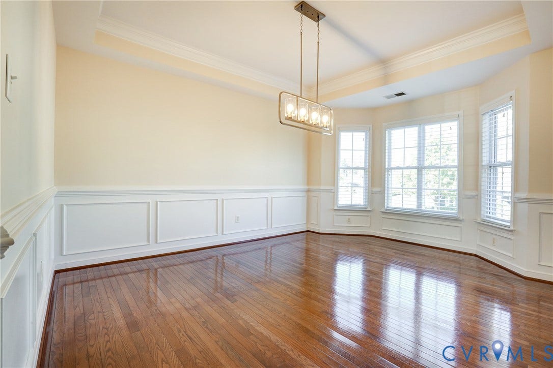 Tray ceiling, wood-finish flooring, wainscoting, bay windows, and a multi-light rectangular chandelier