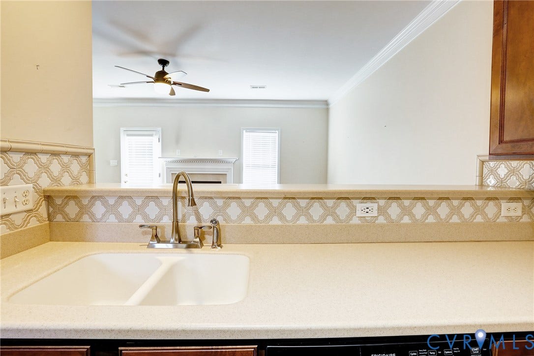 Kitchen featuring a dual-basin sink with a high-arch faucet, patterned tile backsplash, solid-surface countertops, and dark wood cabinetry