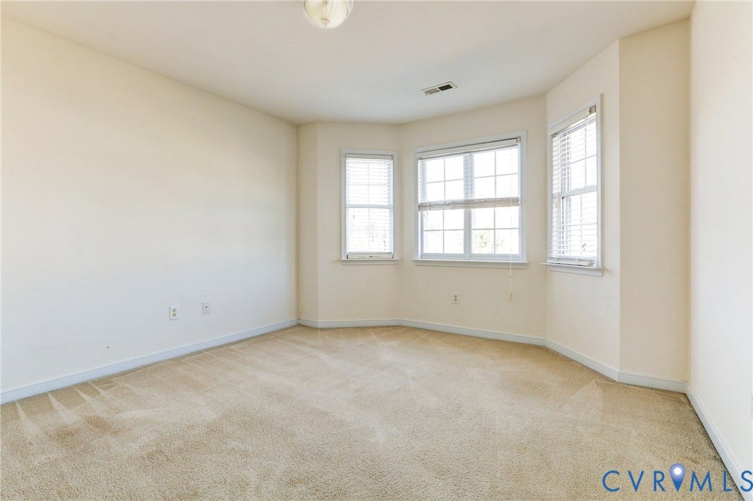 Neutral-toned room featuring a bay window, wall-to-wall carpeting, and flush-mount lighting