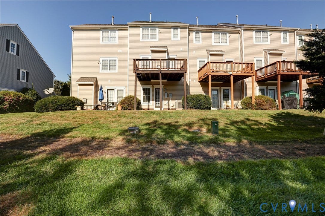 Multi-level townhouse exterior featuring horizontal siding, elevated wooden decks, and grass lawn grounds